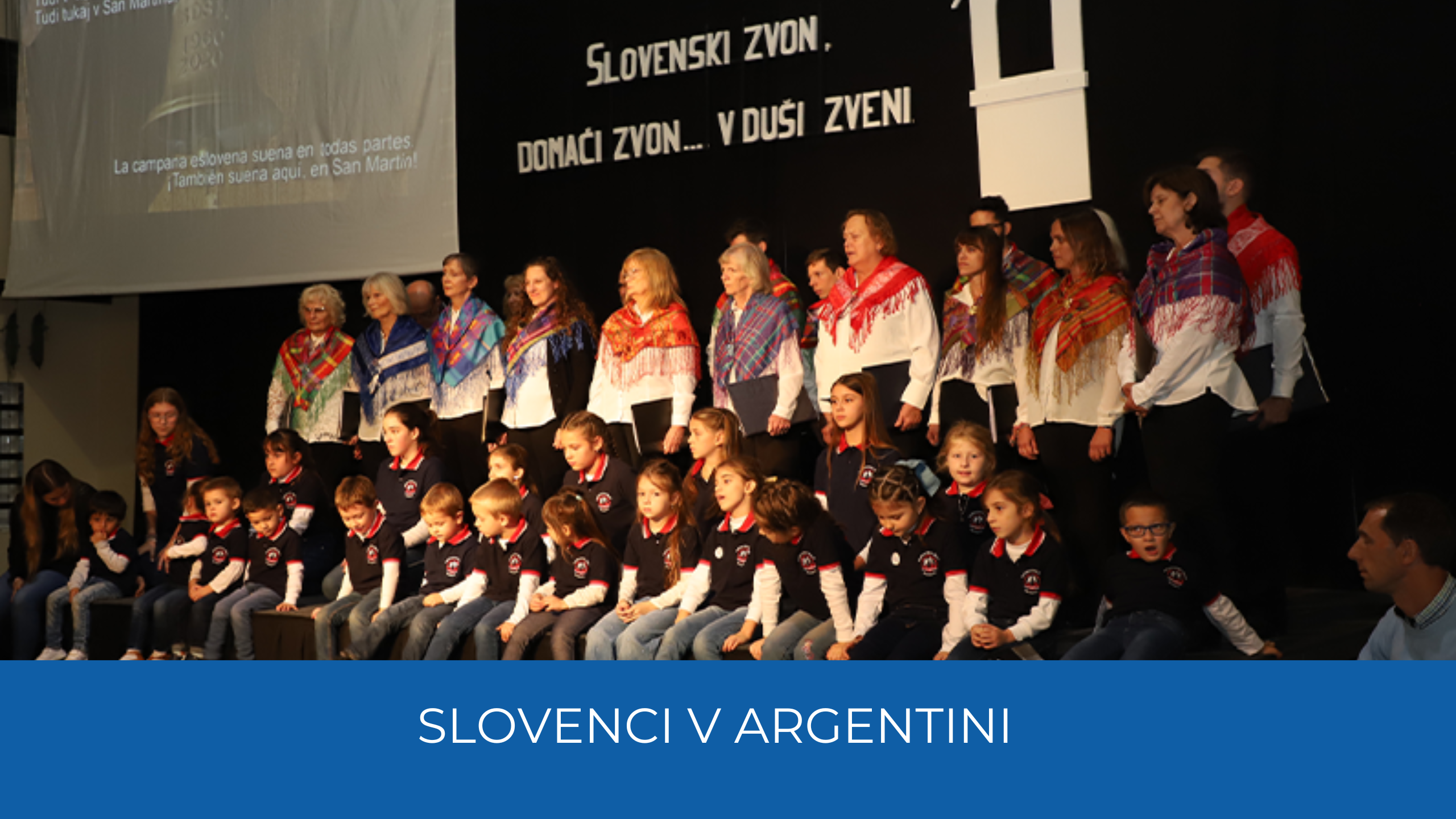 Nastopajoči na odru. Spoidaj modra pasica in napis Slovenci v Argentini.