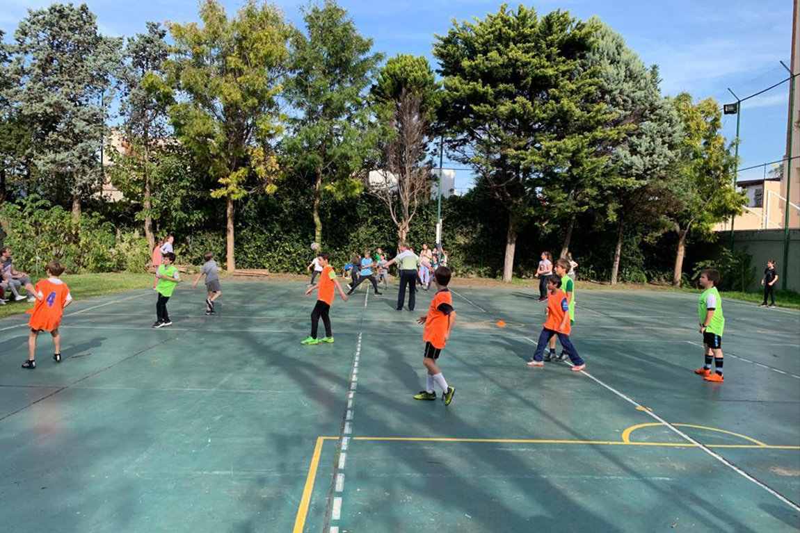 Otroci med tekmo nogometa na šolskem dvorišču. Oblečene imajo rumene in oranžne majice