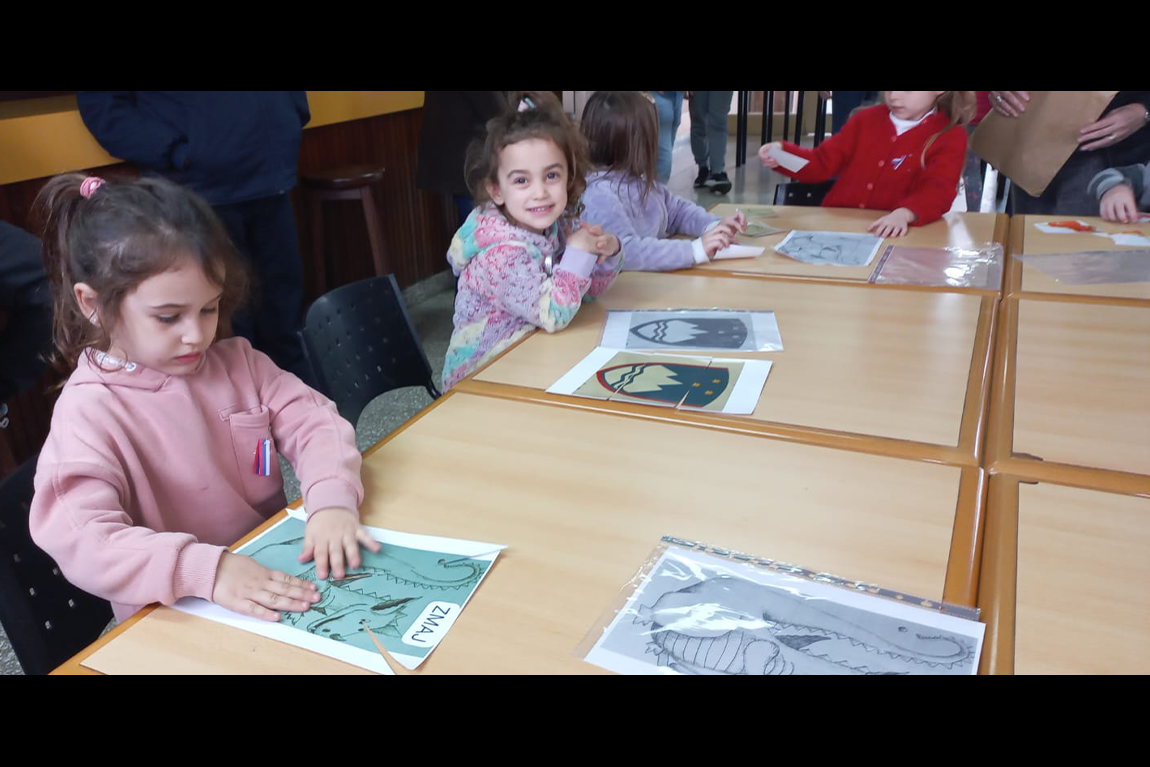 Otroci za mizo barvajo slovenski grb. V ospredju sta dve deklici.