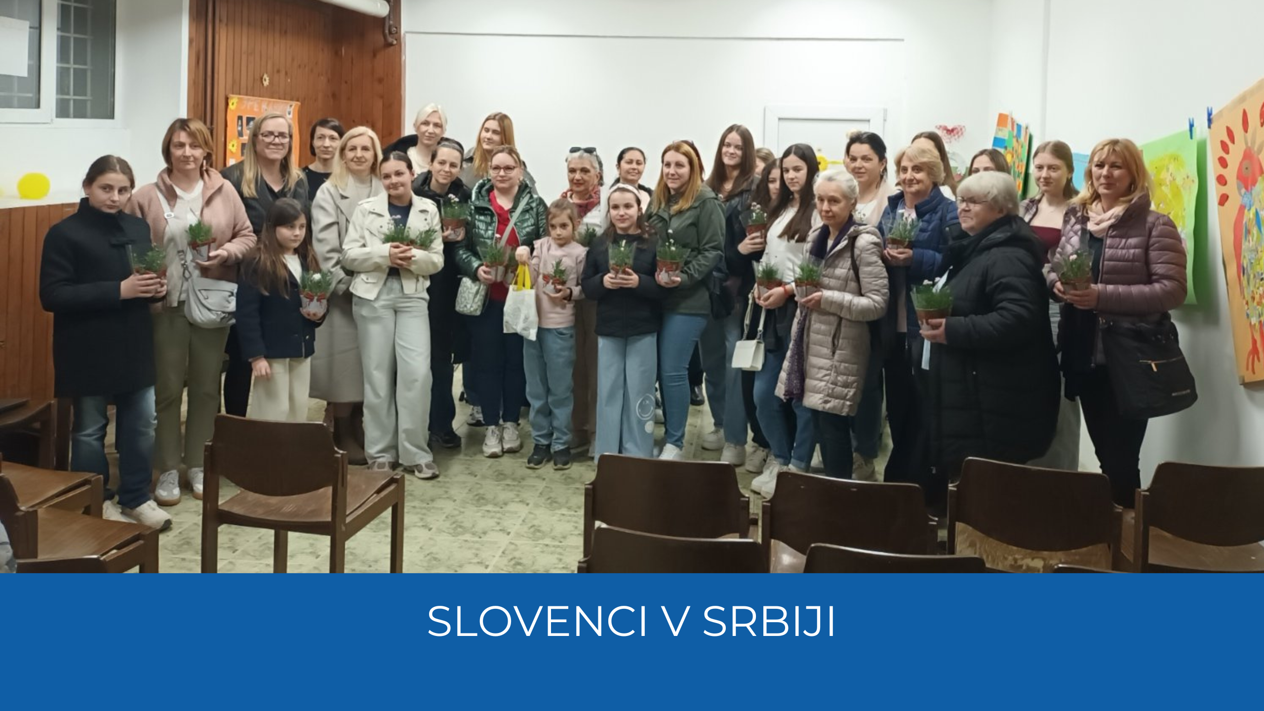 Udeleženci dogodka s šopki. Spodaj na modre traku napis Slovenci v Srbiji.