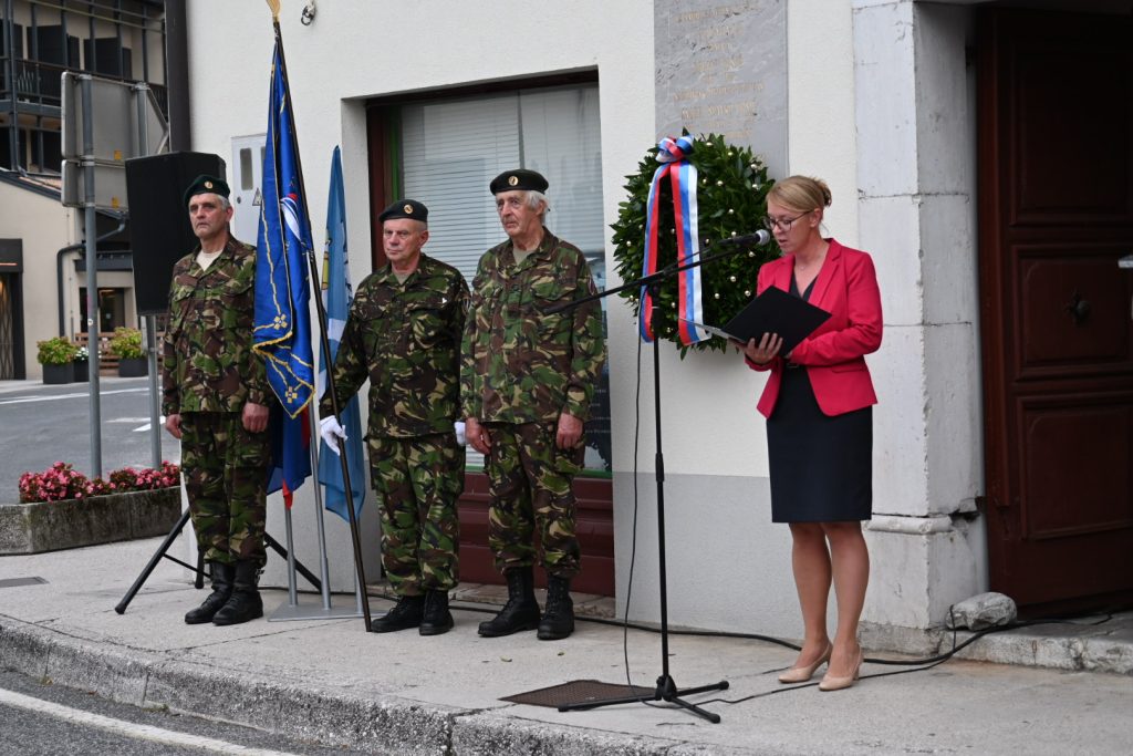 spominski dogodek(1) Državna sekretarka med nagovorm, na levi vojaki in zastave ter venec.